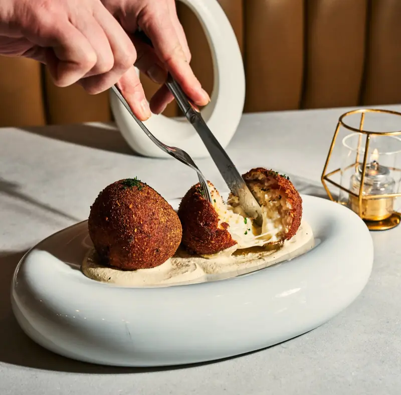 Arancini with melted cheese pulled apart by fork and knife at Five Corners Ristorante